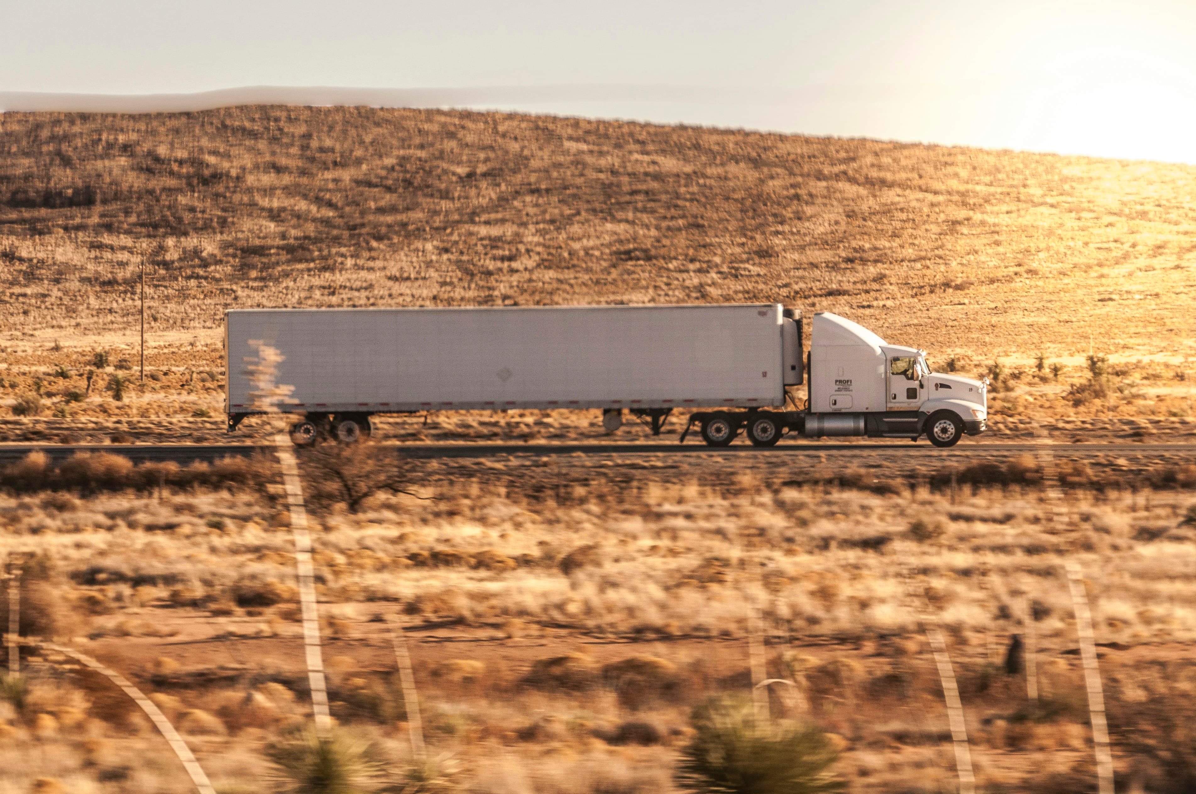 A white semi-truck crossing open desert grassland in warm evening light
