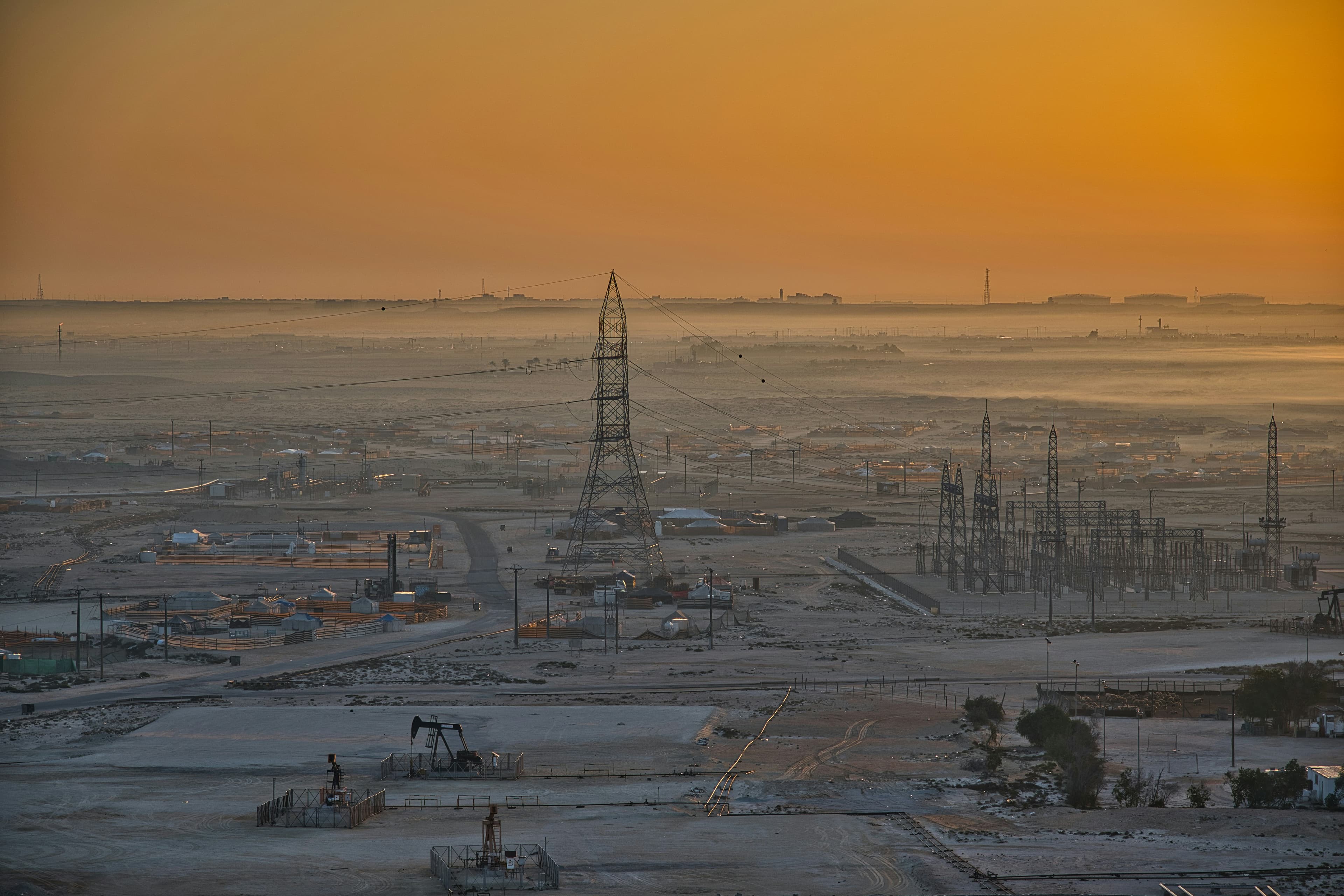 A wide oilfield with pump jacks and power lines under a hazy sunrise