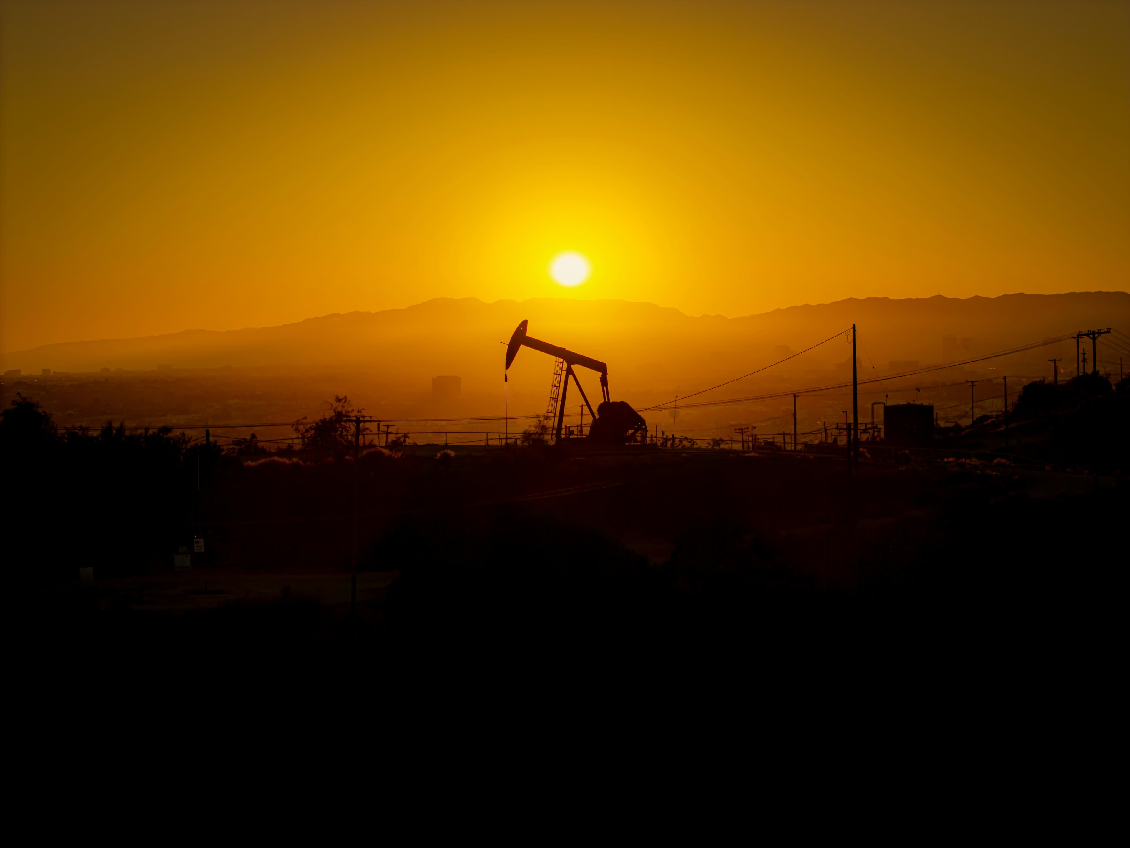 An oil pump jack silhouetted against a hazy orange sunset