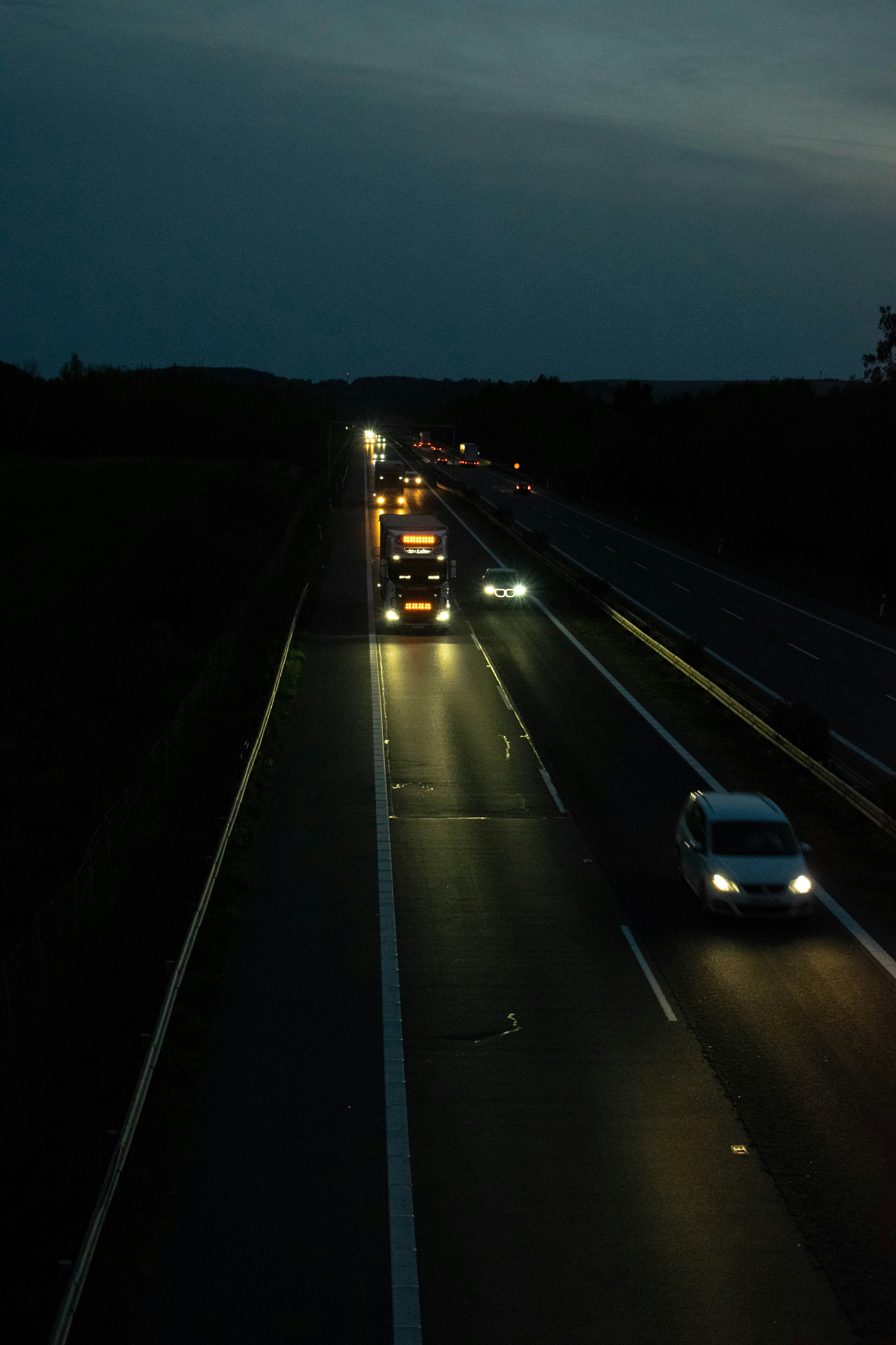 A truck and cars on a highway at night with headlights glowing